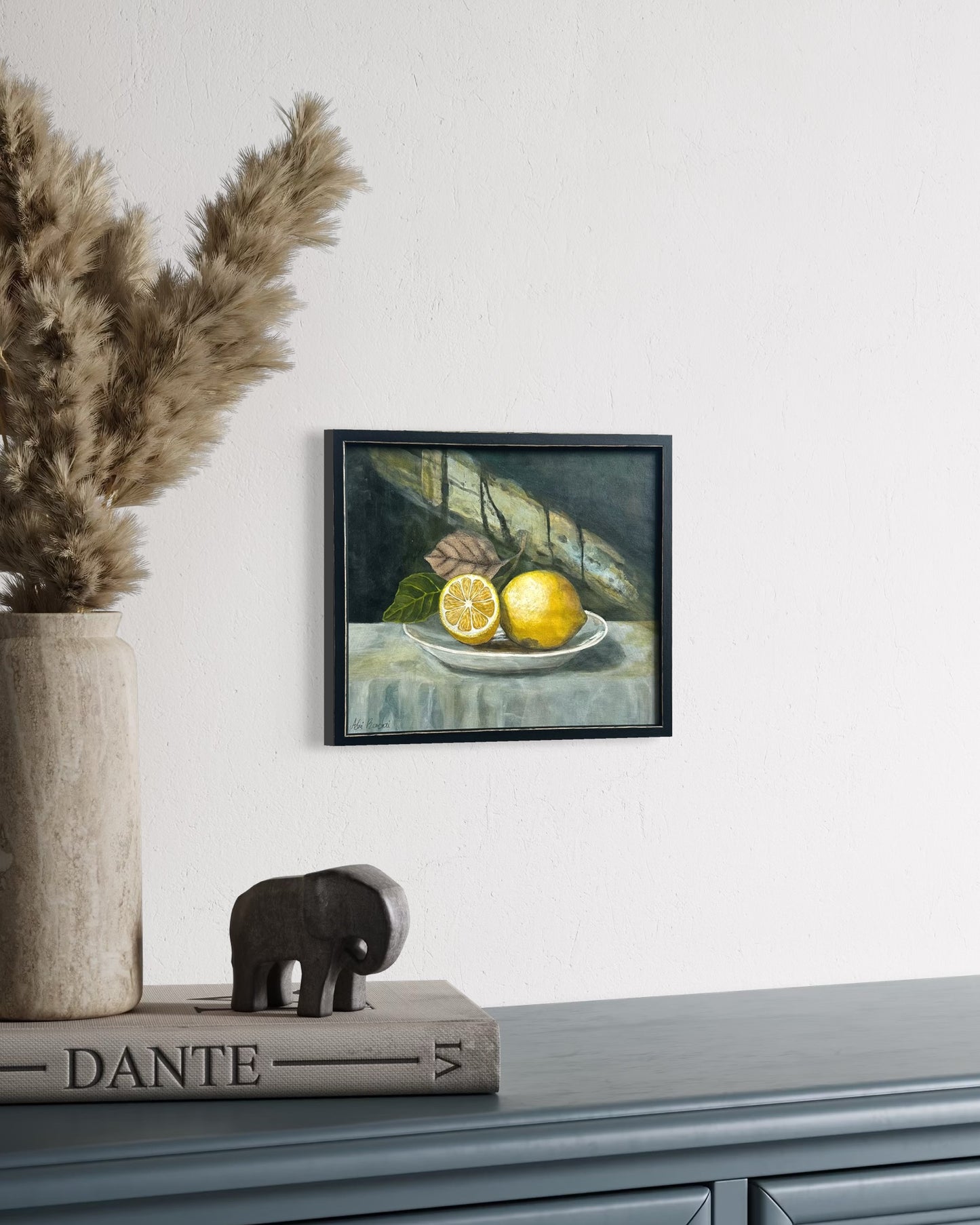 Framed still life painting of lemons on a table with decorative elements on a shelf.